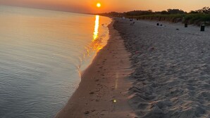 Een strand bij zonsondergang met een rustige zee, een zandstrand en enkele tenten.