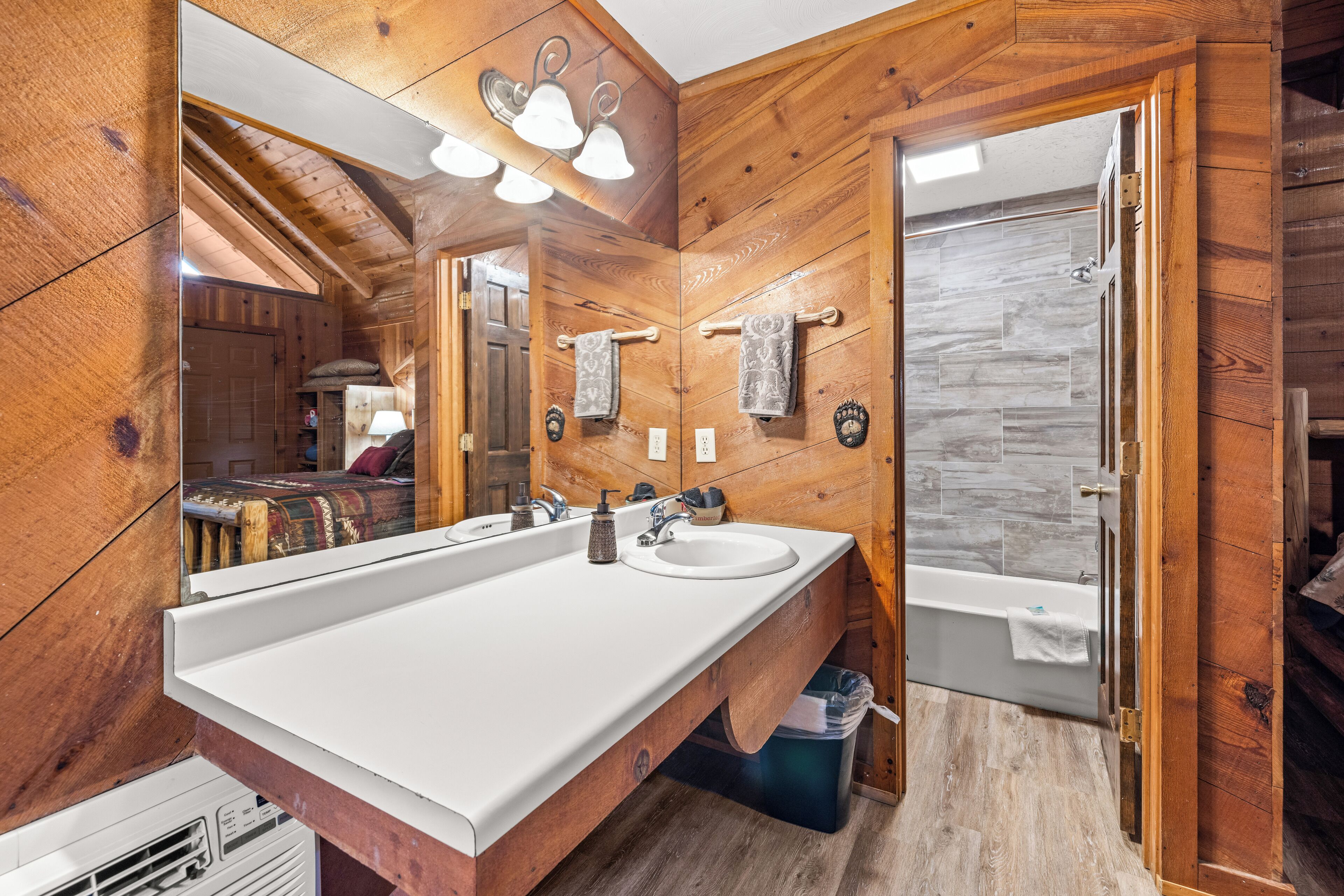 A wooden cabin bathroom with a large mirror, two sinks, a bathtub, and a wooden floor.