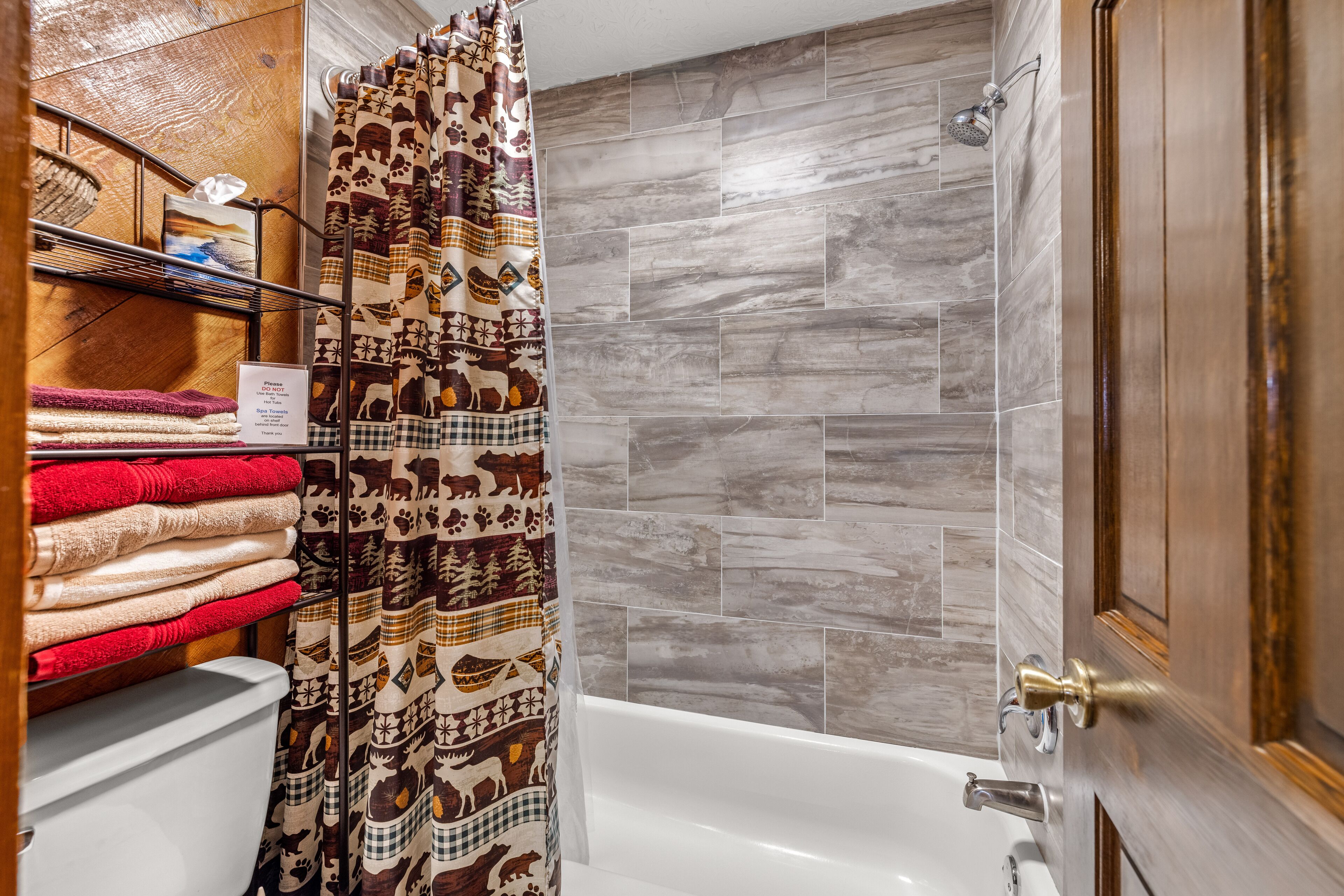 A bathroom with a shower, a toilet, and a towel rack with neatly folded towels.