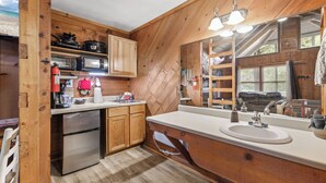 A compact kitchen with wooden walls, a built-in microwave, a sink, and a refrigerator.