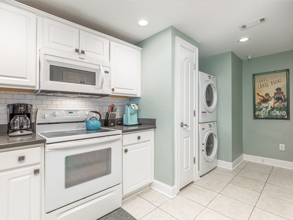 A kitchen with white cabinets, a microwave, an oven, a coffee maker, and a washing machine.