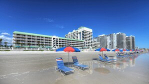 Un hotel sulla spiaggia con diversi edifici, una spiaggia di sabbia e file di lettini con ombrelloni.