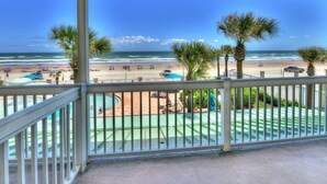 Un balcone con vista sulla spiaggia, palme e zona piscina.
