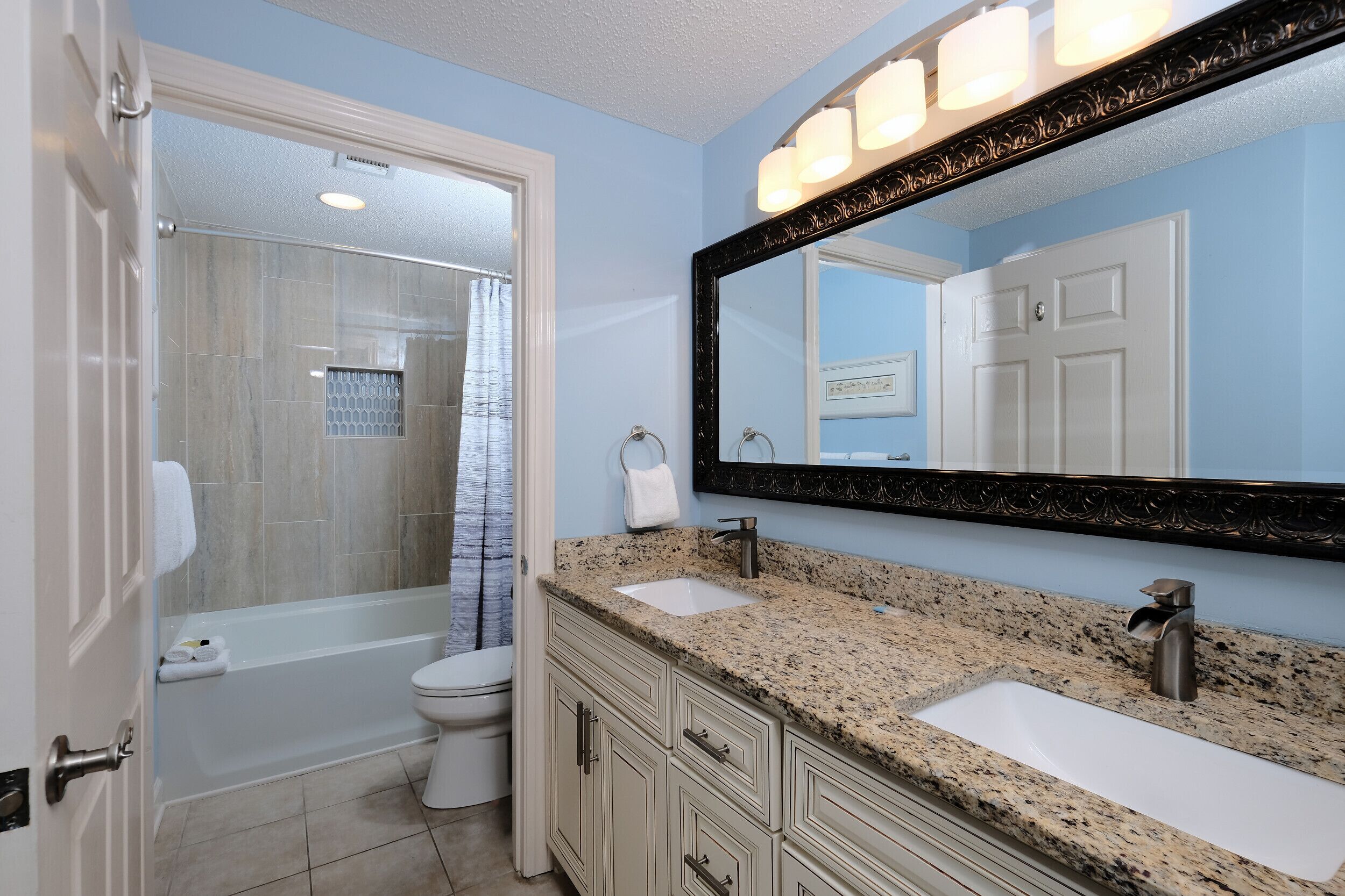 A bathroom with a shower, toilet, and two sinks with a large mirror above.