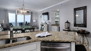 A modern kitchen with granite countertops, stainless steel appliances, and a dining area with a view. - Beautiful 3 Br 3B Gulf Front With Free Wifi Tennis, Pickle Ball, 2 Pools (Orange Beach)