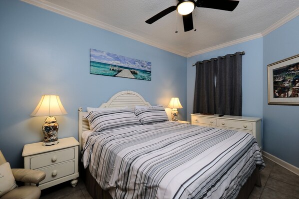 A bedroom with a bed, two bedside tables with lamps, a ceiling fan, and a painting on the wall.