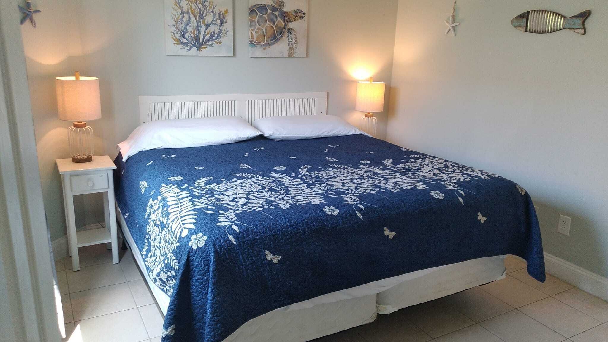 A bed with a blue floral bedspread, two bedside lamps, and artwork on the walls.