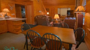 A cozy cabin interior with a wooden dining table, chairs, a sofa, and a television.