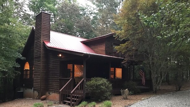 A rustic cabin with a metal roof, a front porch, and a gravel driveway.
