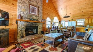 A cozy log cabin interior with a stone fireplace, leather furniture, and a large rug with animal patterns.