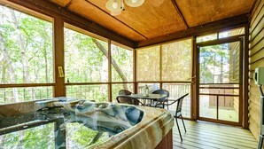 A hot tub on a wooden deck with a table and chairs, surrounded by large windows.