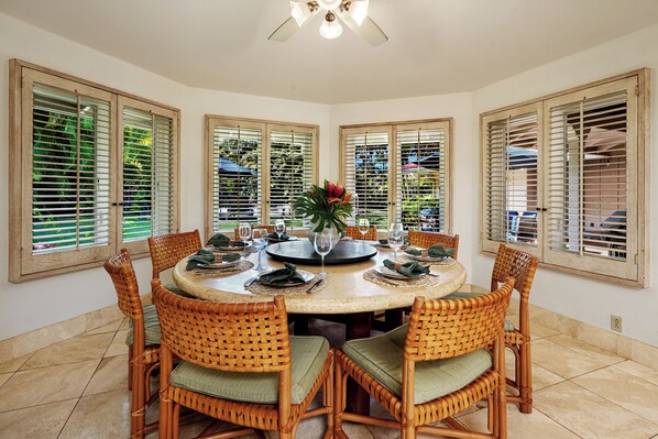 A dining area with a round table, wicker chairs, and a ceiling fan. - Loke Lani + Guest 'Ohana | Romantic Poipu Retreat w/ Private Pool & Luxury Comfort (Koloa)