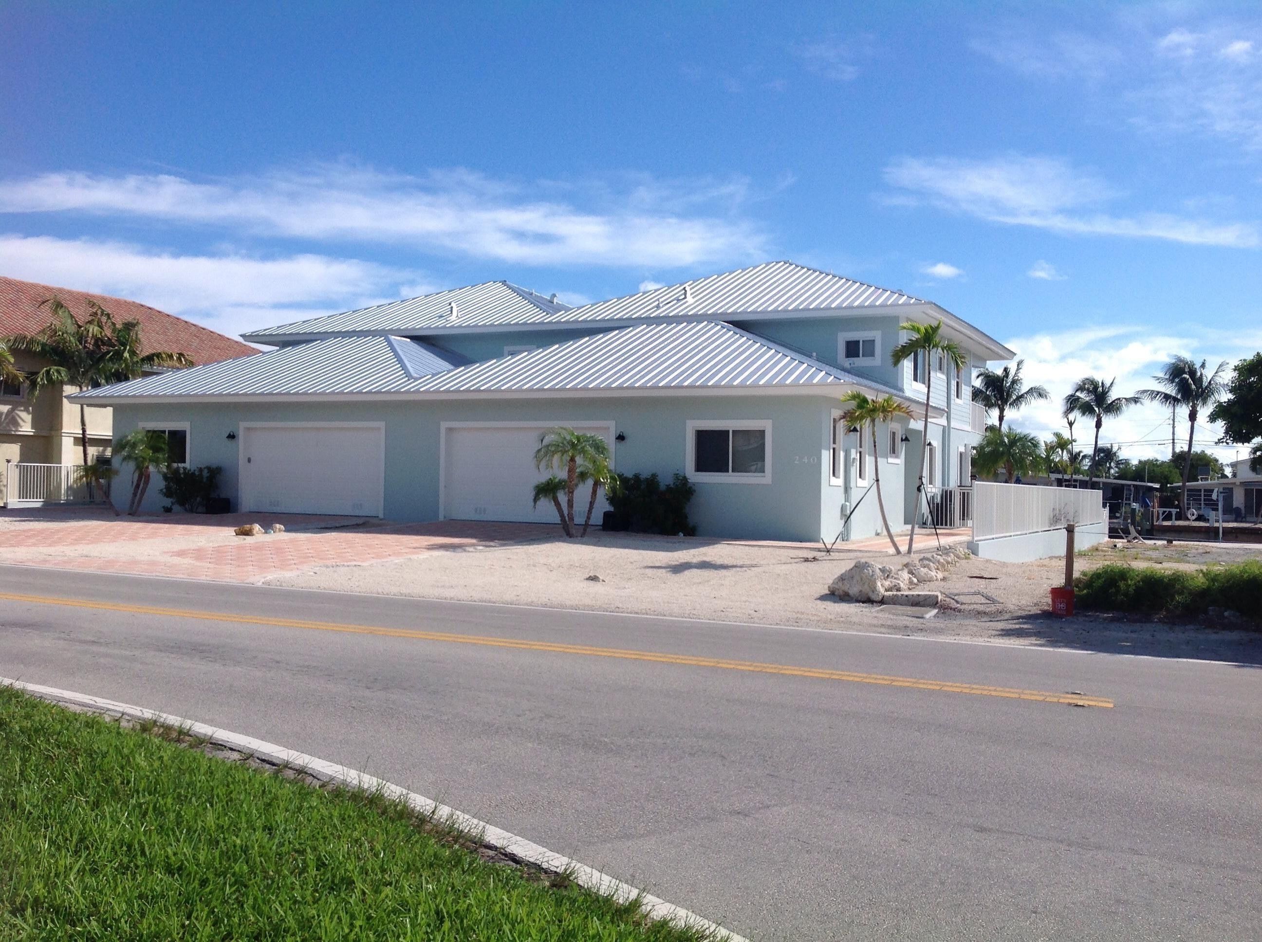 A two-story house with a light blue exterior, a metal roof, and two garage doors.
