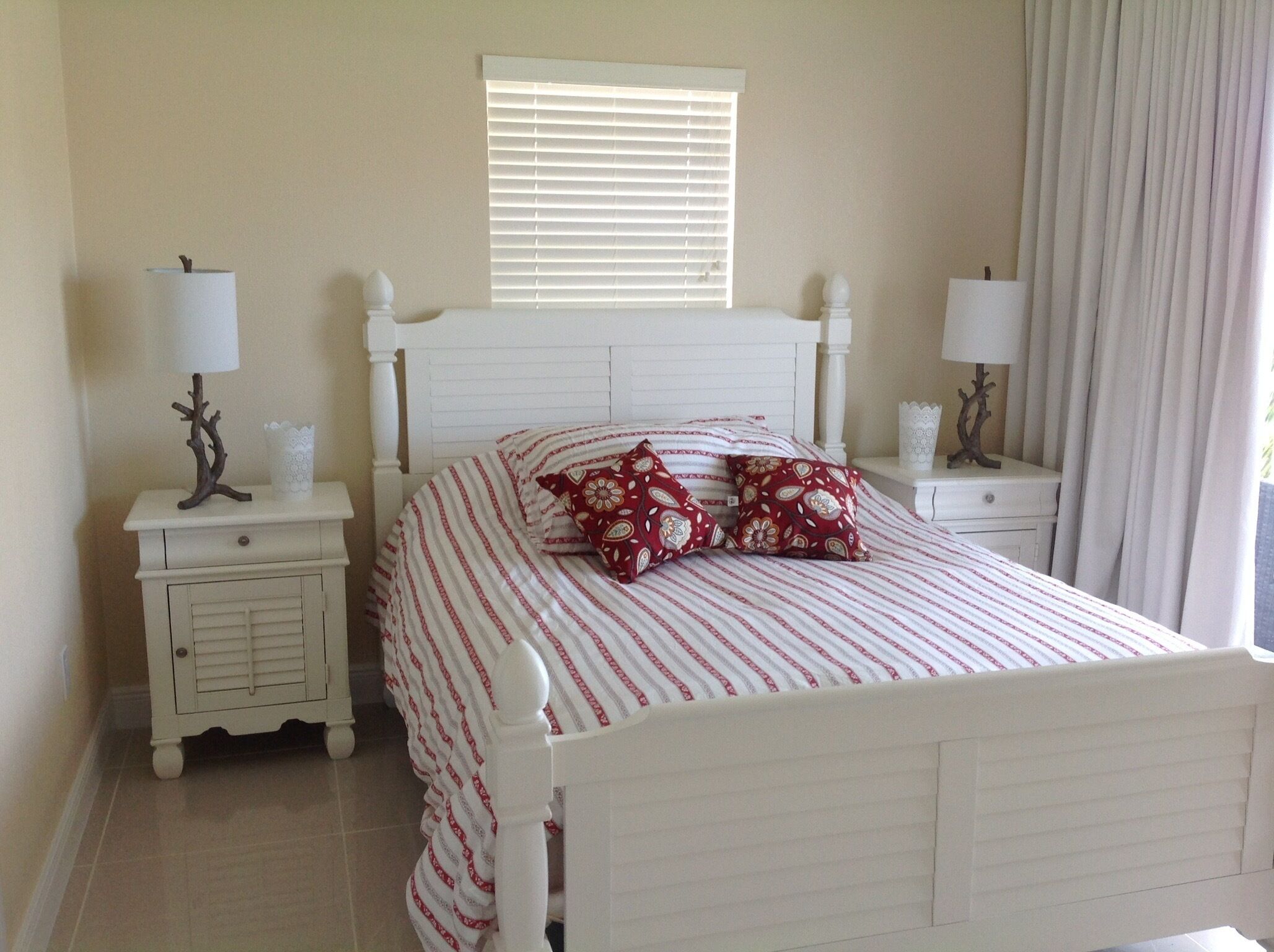 A bedroom with a white bed, striped bedding, two nightstands with lamps, a window with blinds, and a curtain.