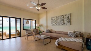 A spacious living room with a large sofa, a coffee table, and a ceiling fan. There is a large window with a view of the beach. - LUXURY BEACHFRONT VILLA  Includes 3 Pools, Wifi, Best Snorkeling & Kayaking Bay (Tulum)