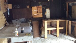 Una habitació desordenada amb un sostre deteriorat, una taula de fusta i diversos objectes sobre la taula, com ara una ampolla i una llauna.