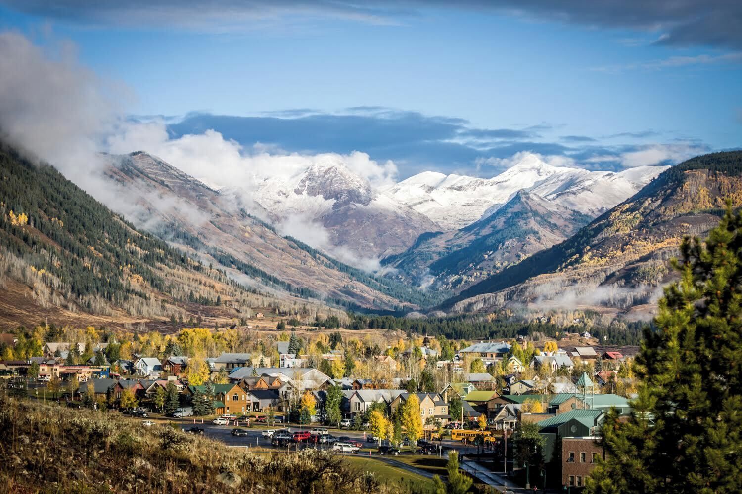 Une ville nichée dans une vallée, avec des montagnes en toile de fond, et entourée d’arbres aux couleurs automnales.