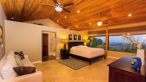 A bedroom with a bed, a desk, a chair, a ceiling fan, and a view of the outdoors.