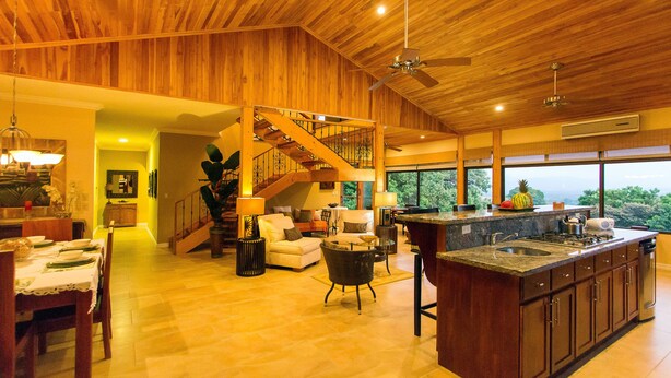A spacious living area with a wooden ceiling, a kitchen with a large island, and a staircase leading to an upper level.