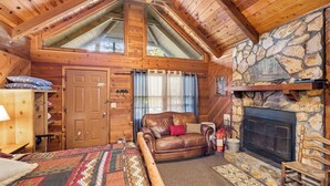 A cozy log cabin interior with a stone fireplace, wooden ceiling, and a large bed with a patterned bedspread.