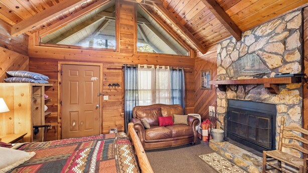 L’intérieur d’un chalet confortable, avec une cheminée en pierre, un plafond en bois et un grand lit recouvert d’une courtepointe à motifs.