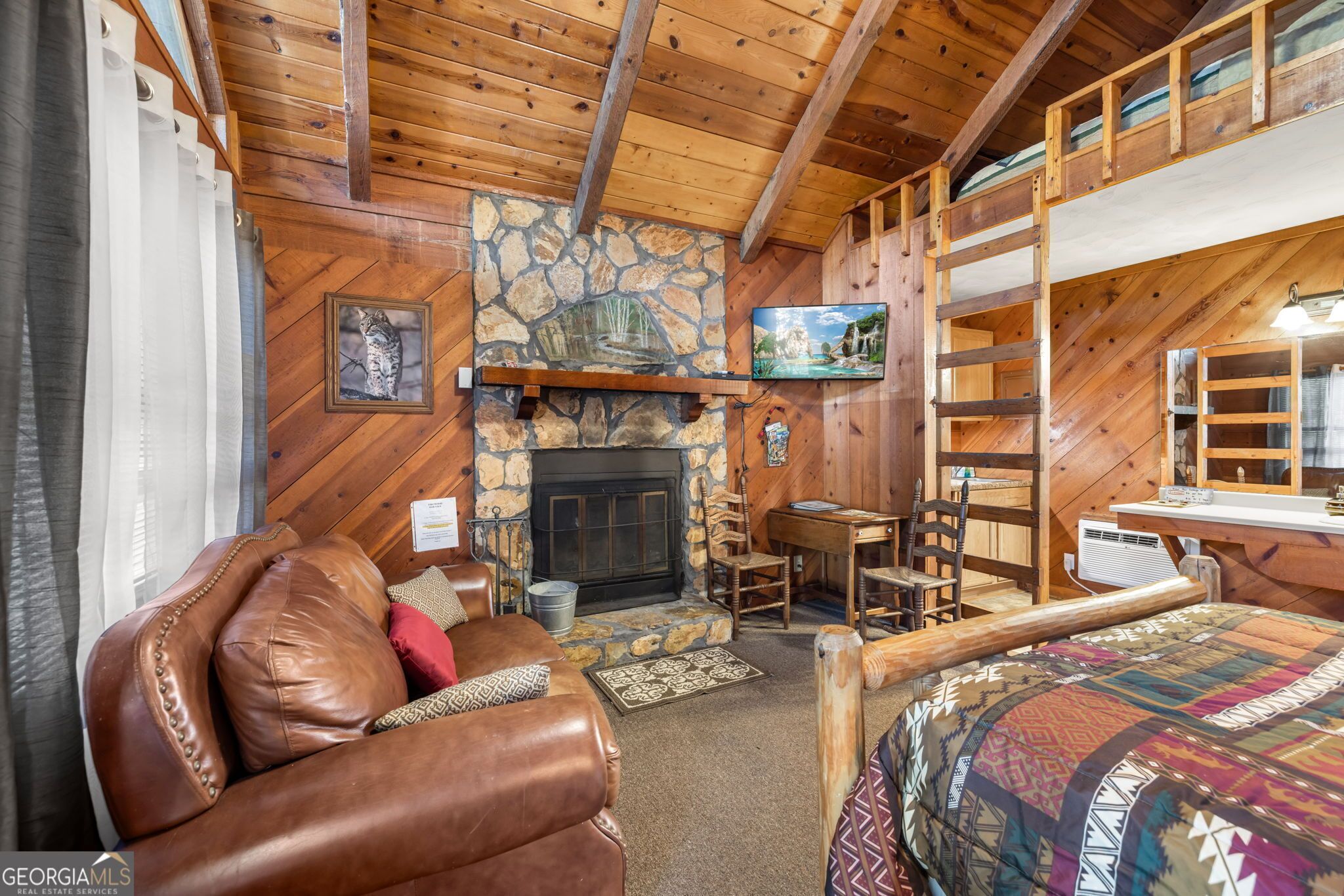 Un intérieur de chalet chaleureux avec une cheminée en pierre, un fauteuil inclinable en cuir et un lit superposé.