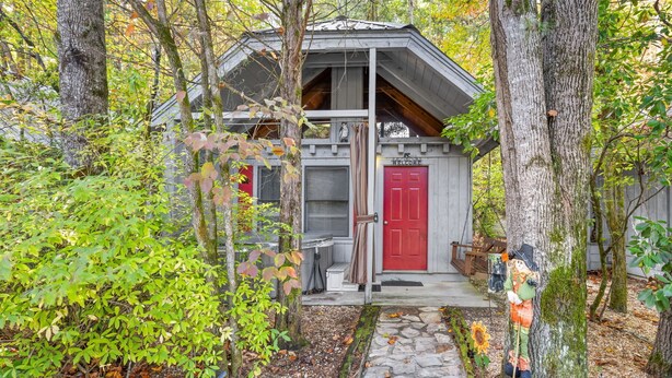 A rustic cabin with a red door, surrounded by trees and a stone pathway.