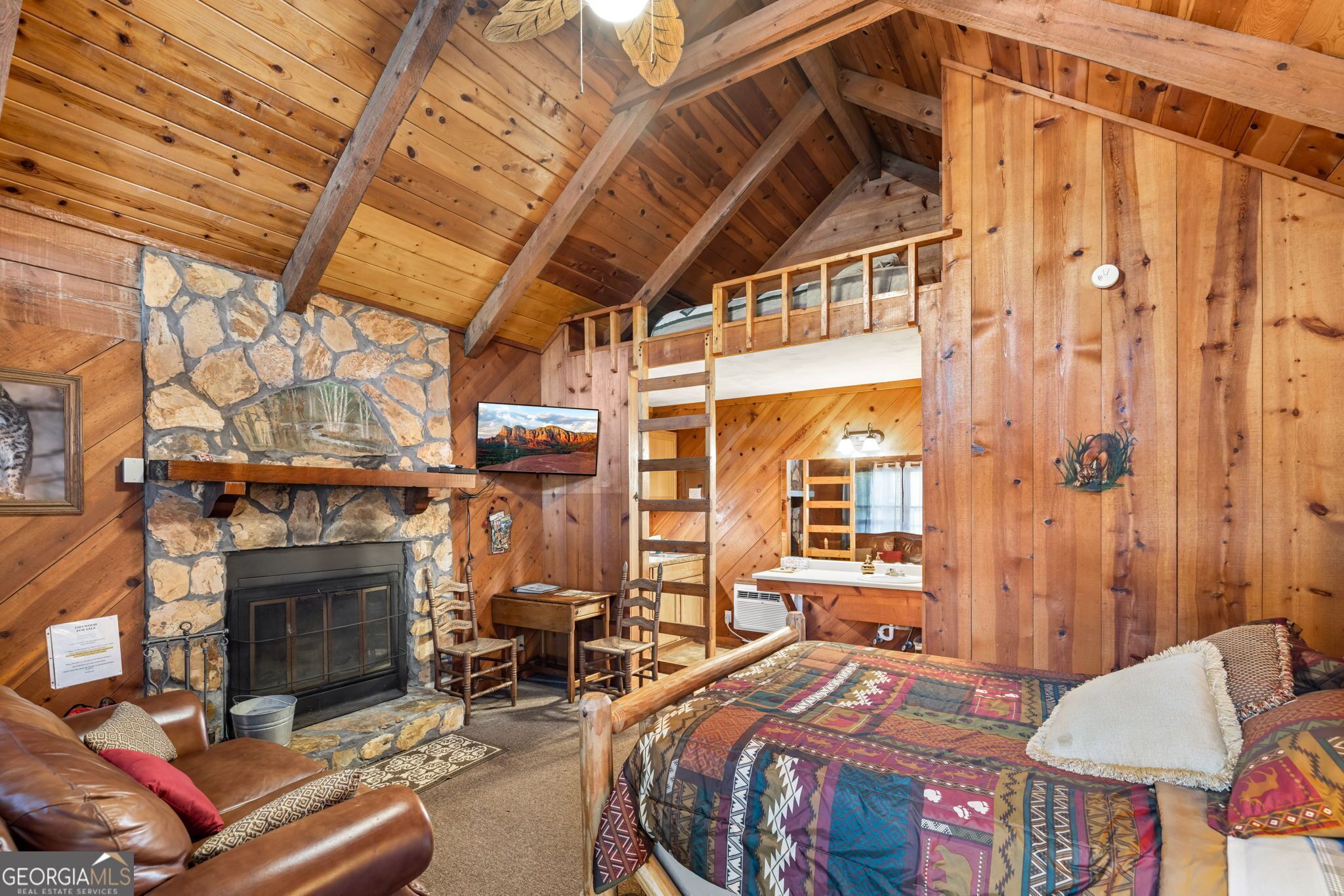 A cozy cabin interior with a stone fireplace, a loft bedroom with a bunk bed, and a dining area.