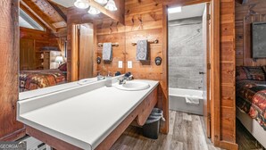 Ein Badezimmer einer Holzhütte mit einem großen Spiegel, einem Waschbecken, einer Badewanne und einer Dusche.