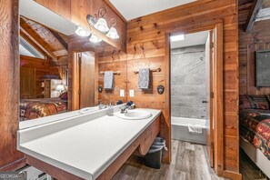Un baño de cabaña de madera con un espejo grande, un lavamanos, una bañera y una ducha.