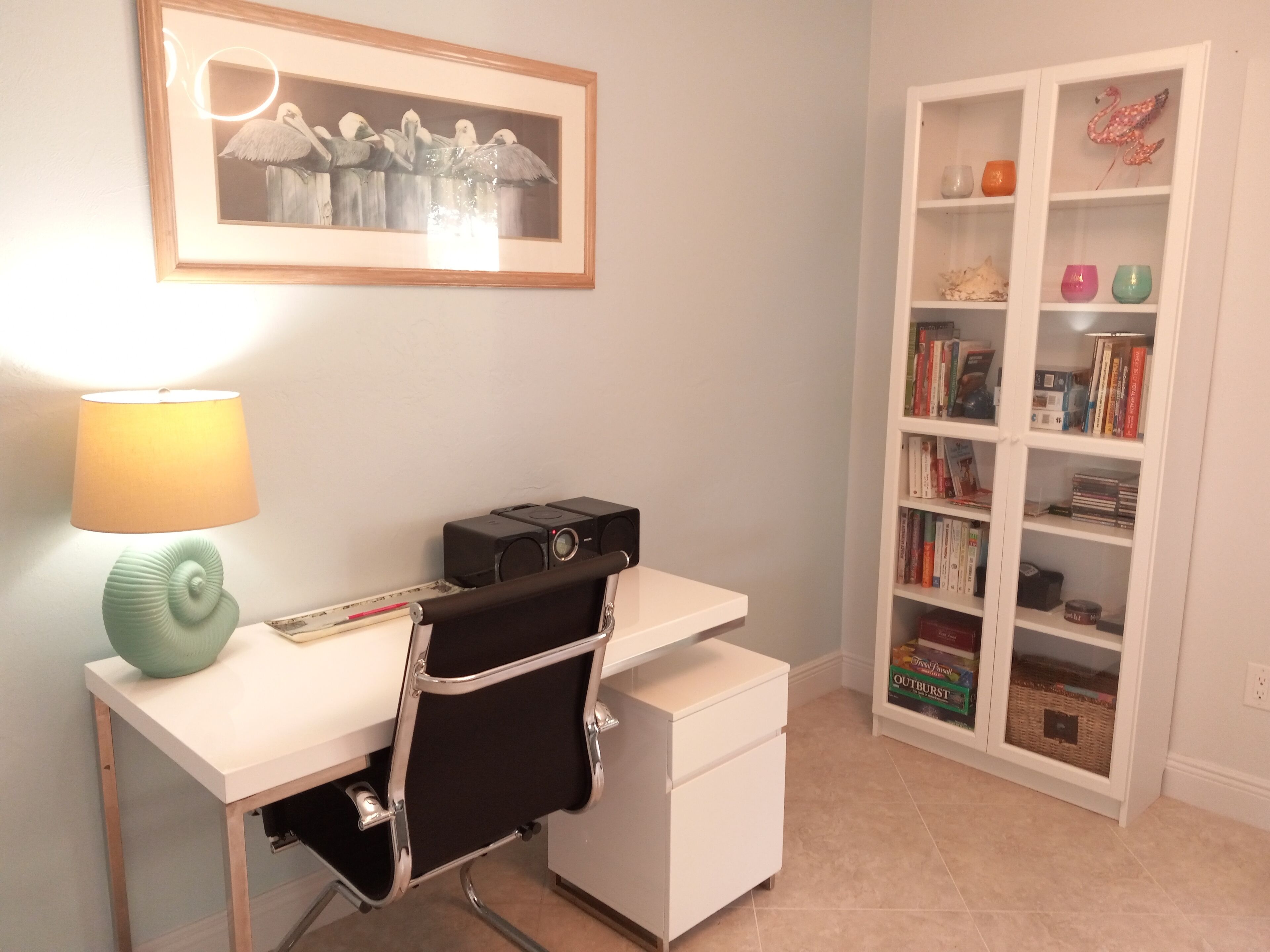 A study area with a desk, chair, lamp, bookshelf, and framed artwork.