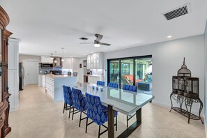 Een moderne keuken met witte kastjes, een centraal eiland en blauwe stoelen met een patroon.
