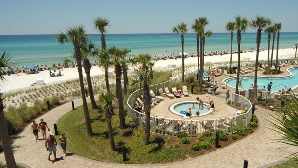 Un complexe hôtelier doté d’une piscine entourée de palmiers, d’une plage et offrant une vue dégagée sur l’océan.