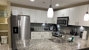 Une cuisine moderne dotée de plans de travail en granit, d’appareils électroménagers en acier inoxydable et de luminaires suspendus.