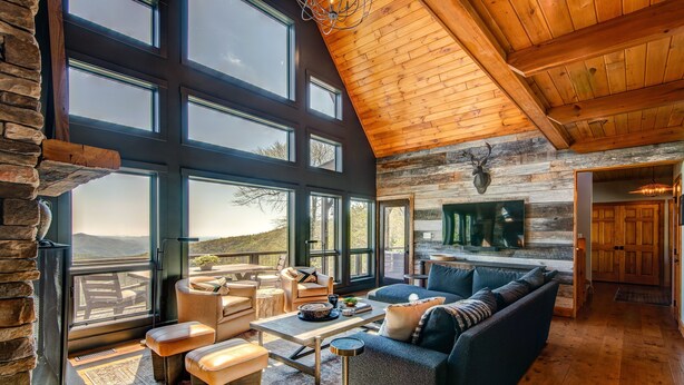 A spacious living room with a large window, a fireplace, and a cozy seating area. - Owls Nest - Pool Table, hot tub, views, Indoor & Outdoor Fireplaces (Blowing Rock)