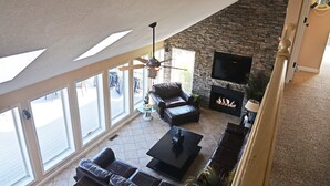 A spacious living room with a stone fireplace, leather sofas, a coffee table, and a ceiling fan. - Luxury Lakefront Estate! 6BR 4.5BA, Private Dock,Ramp, Lakeside Firepit & More! (Greenwood)