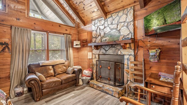 A cozy cabin interior with a stone fireplace, wooden walls, a leather sofa, and a wooden staircase.