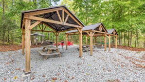 A covered picnic area with benches and picnic tables in a forest setting.