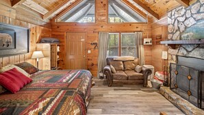 A log cabin interior with a loft bedroom, a fireplace, and a stone wall.