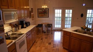 A kitchen with wooden cabinets, a microwave, a stove, and a dining area with a chair and table. - Marshbreeze...on Tidal Creek with Marsh View (Darien)