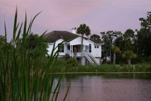 Situated near a serene lake, this charming home features a spacious porch and a staircase leading to an upper level surrounded by lush greenery.