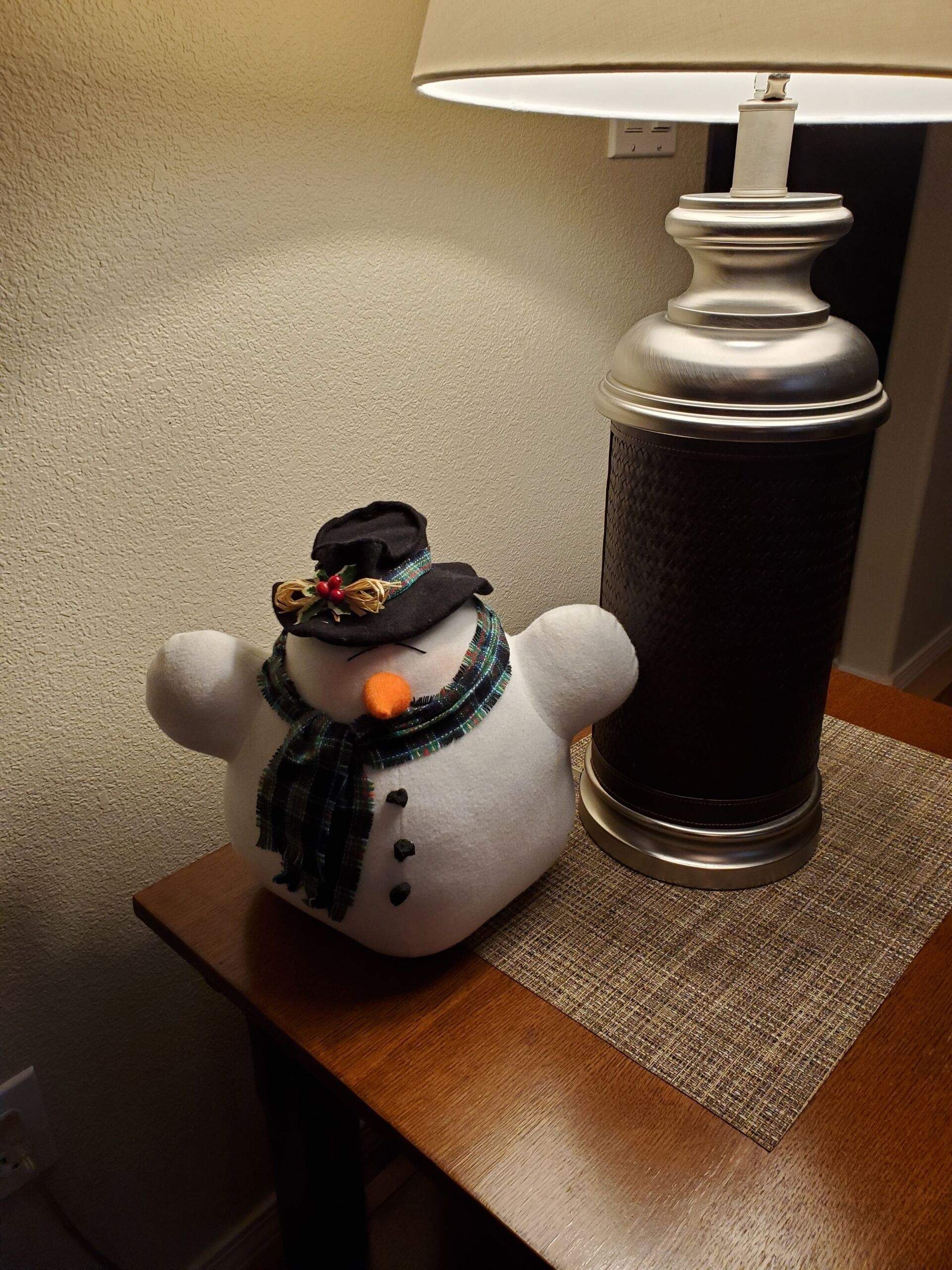 A snowman figurine on a wooden table next to a lamp.