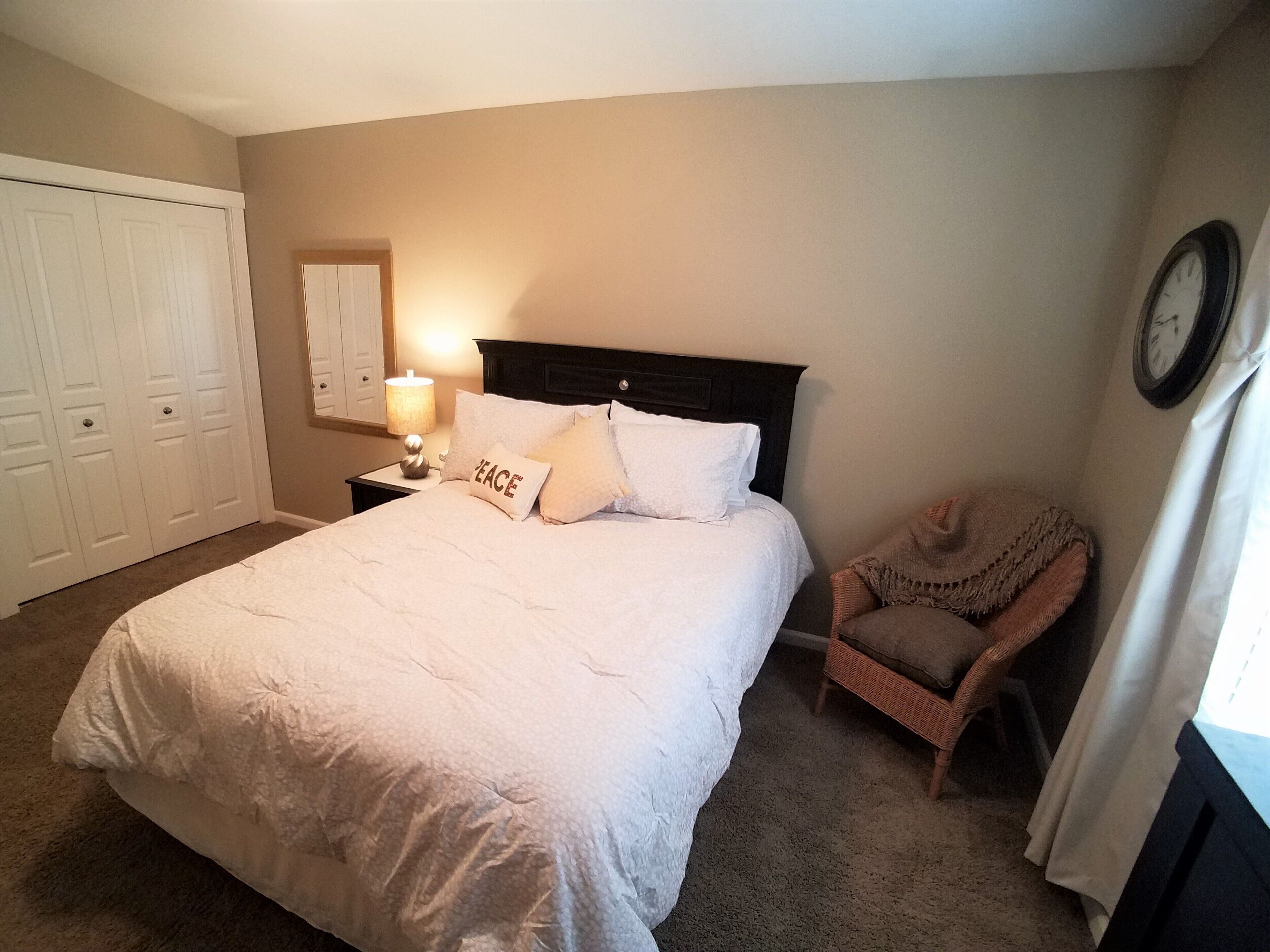 Un dormitorio con una cama grande, una mesita de noche con lámpara, una silla y un armario.
