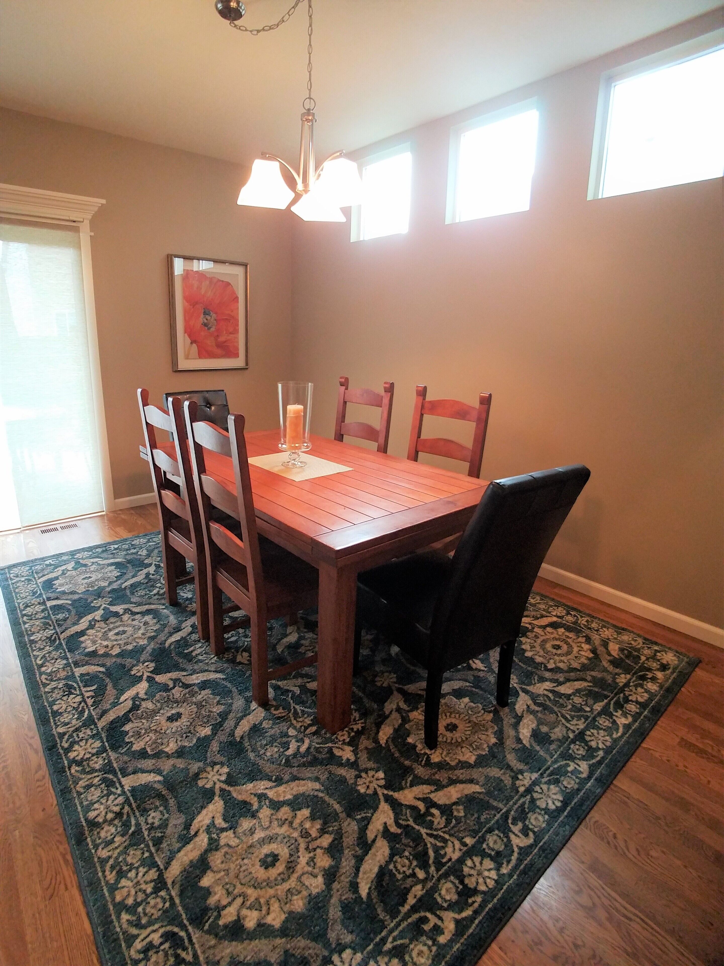 A dining area with a wooden table and chairs, a patterned rug, and a pendant light.