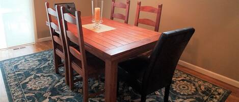 A dining area with a wooden table and chairs, a patterned rug, and a pendant light.