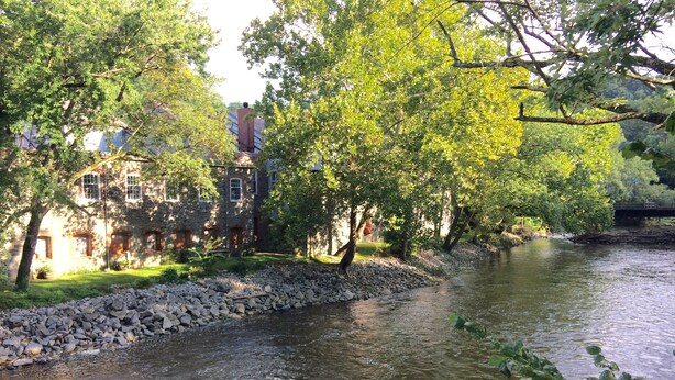 A river with a stone embankment and trees, a stone building with windows and a chimney, and a bridge in the background. - Private Suite w/sitting room  in the heart of Brandywine Valley (Wilmington)