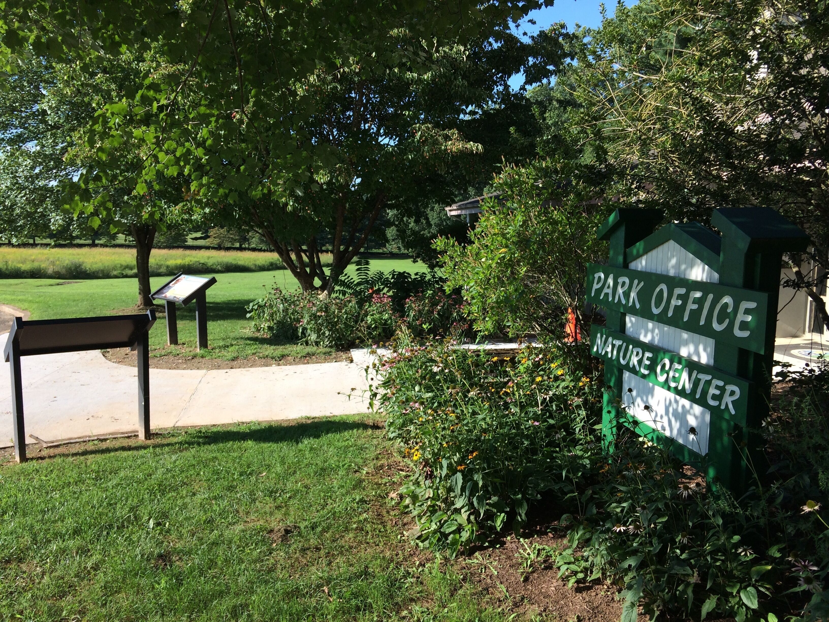 A park office sign with a nature center label, surrounded by greenery and a pathway.