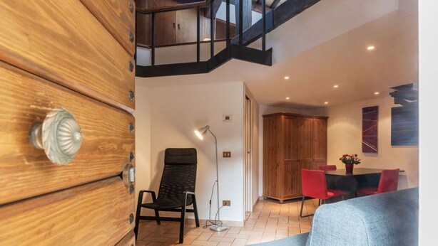 A modern interior with a wooden wardrobe, a black chair, a grey sofa, a dining table with red chairs, and a staircase. - Amazing studio in Campo de' Fiori - Air Conditioning - Free Wi-Fi (Rome)