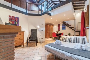 A modern hotel room with a bed, a desk, a chair, and a staircase leading to an upper level.