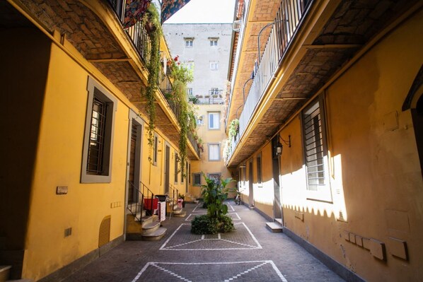 A narrow alleyway with yellow buildings, a small tree, and a staircase leading to an upper floor.